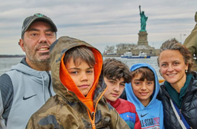 Family on the bow of a classic boat with the Statue of Liberty Behind them for a NY Harbor Sightseeing Boat Tour