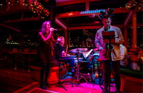 several band members on a stage performing music on the Yacht Manhattan II