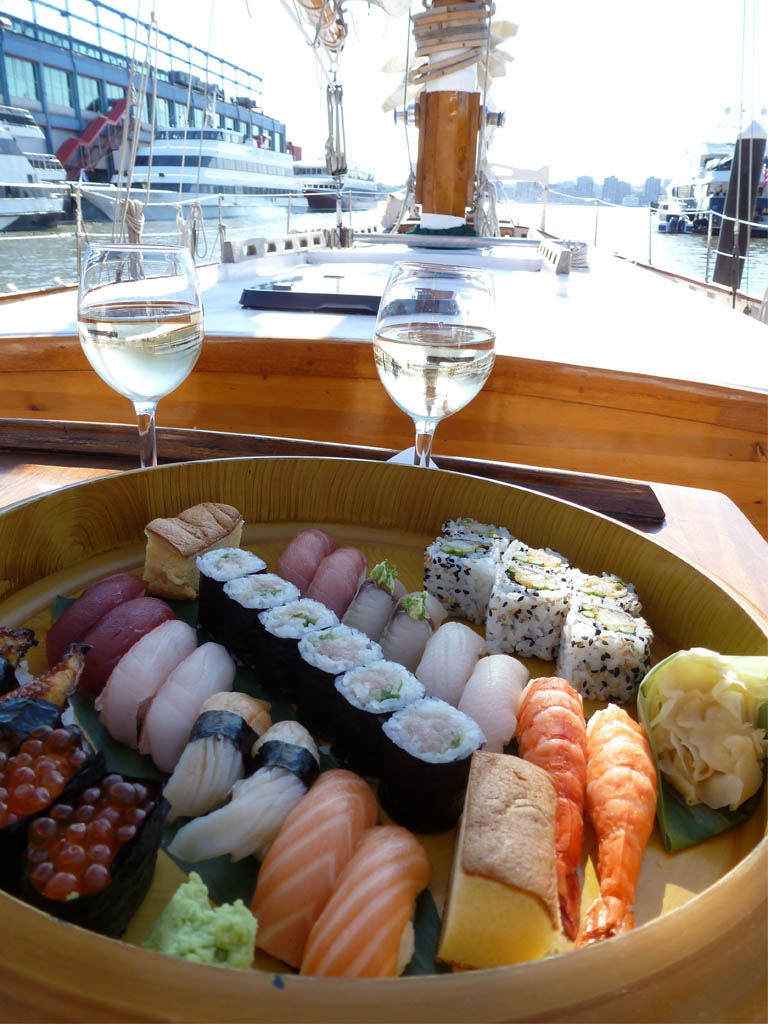 an assortment of different types of sushi in a bowl, with two glasses of wine half filled