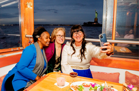 three woman on a bench leaning in for a selfie aboard yacht Manhattan in NY Harbor