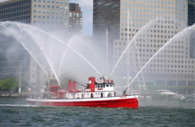 the John J Harvey fireboat sailing down the New York river, shooting water from its cannons
