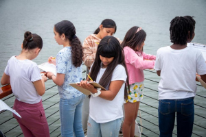 group of kids writing on notebooks overlooking on a pier