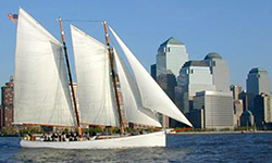 the schooner adirondack cruising down a river with a city in the background