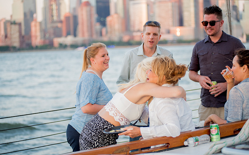 Group of friends standing on the decks of Schooner America 2.0 looking off to the Statue of Liberty