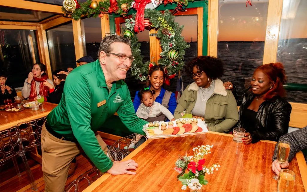 Crew member serving a cheese plate to customers on a Holiday City Lights Cruise in NYC