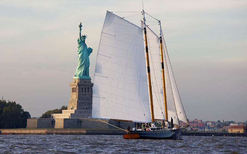 the schooner america 2.0, sailing past the statue of liberty, down a river