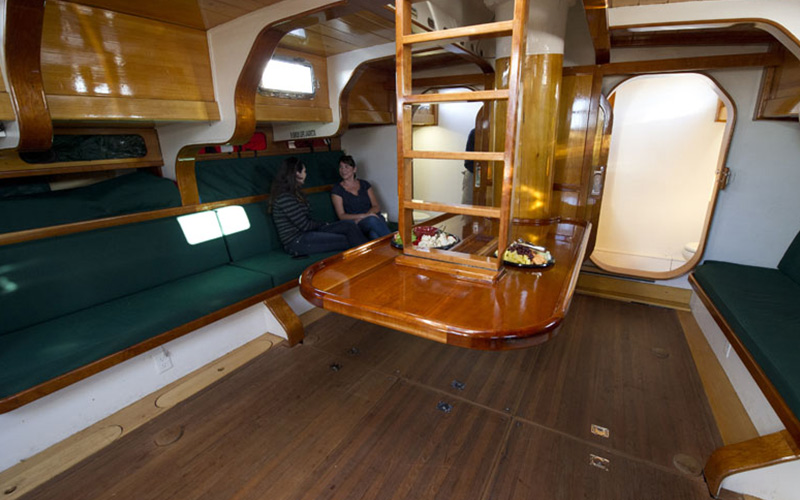 an interior view of the schooner america 2.0, with two passengers sitting on a bench inside