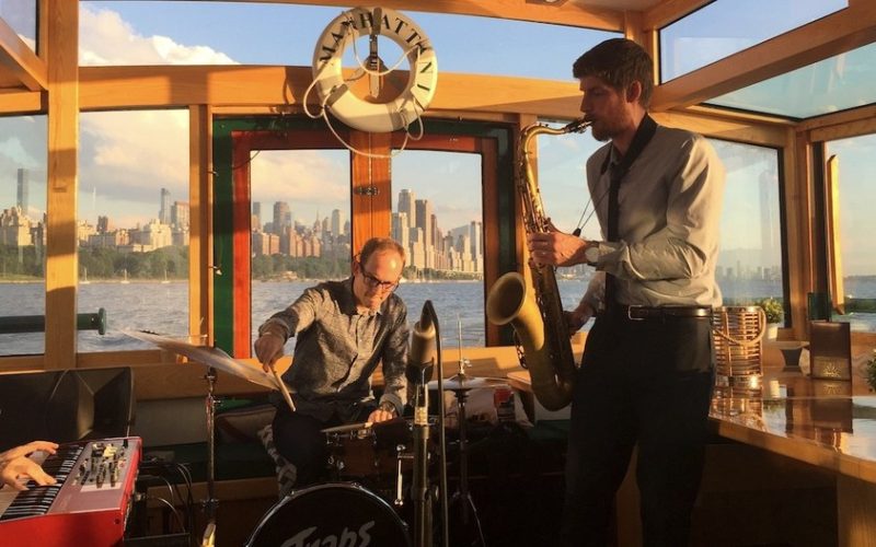 Live band playing holiday music on Yacht Manhattan II with a landscape of the city in the background