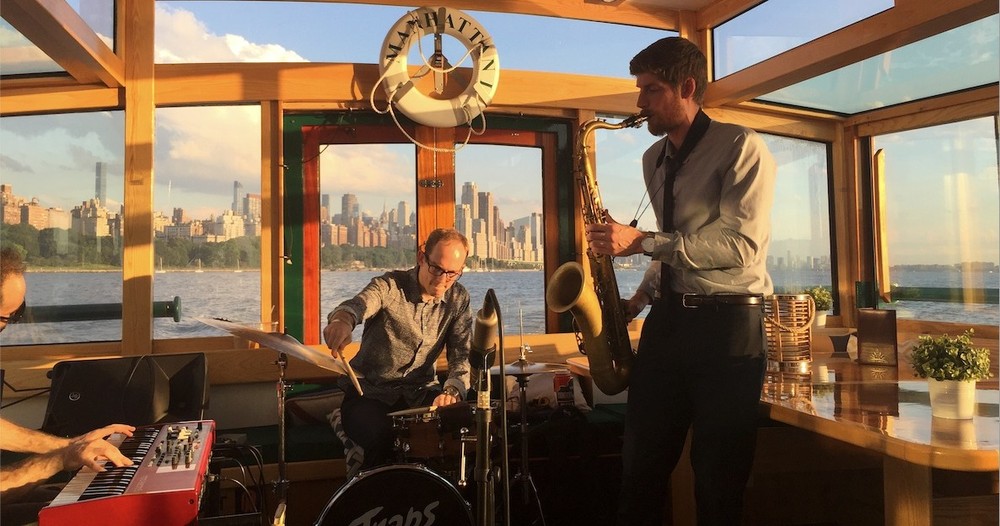 Live band playing holiday music on Yacht Manhattan II with a landscape of the city in the background