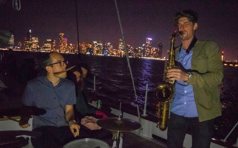 Live band playing holiday music on Yacht Manhattan II outside with a lit city in the background