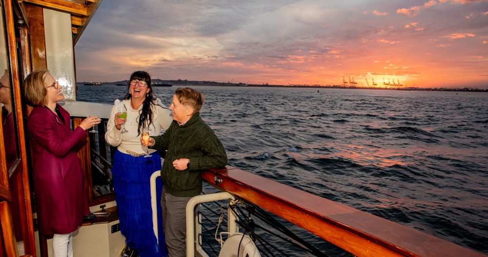 SailNYC_Sunset-Holiday_Slider-5 Three guests toast with pink skies hovering over the water