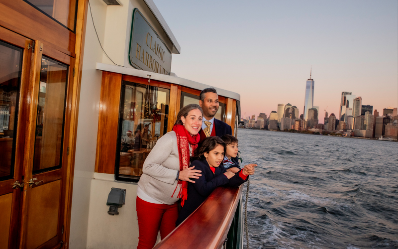 Family on the decks of a classic yacht looking out at the NYC Skyline