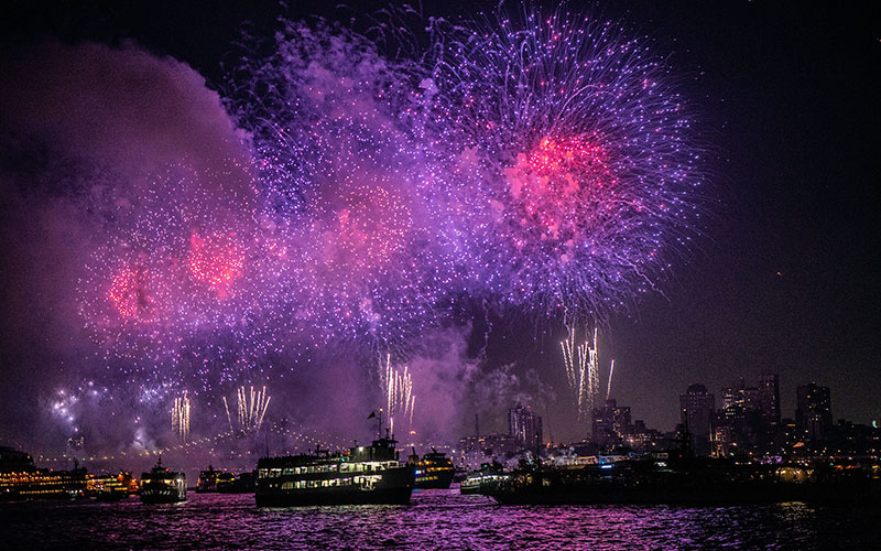 a river full of boats and fireworks shooting off in the distance