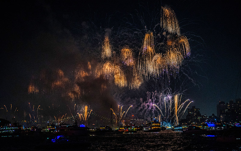 a river full of fireworks and boats, with a city full of lights