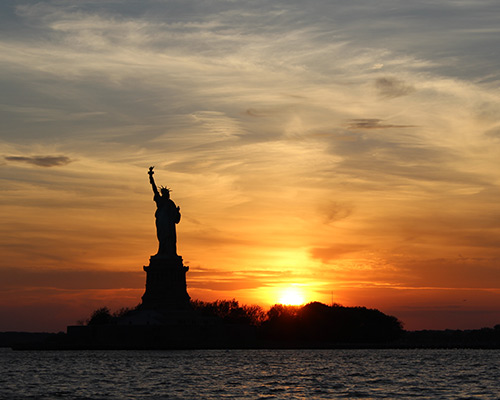 a sunset in the distance across a river, with the statue of liberty