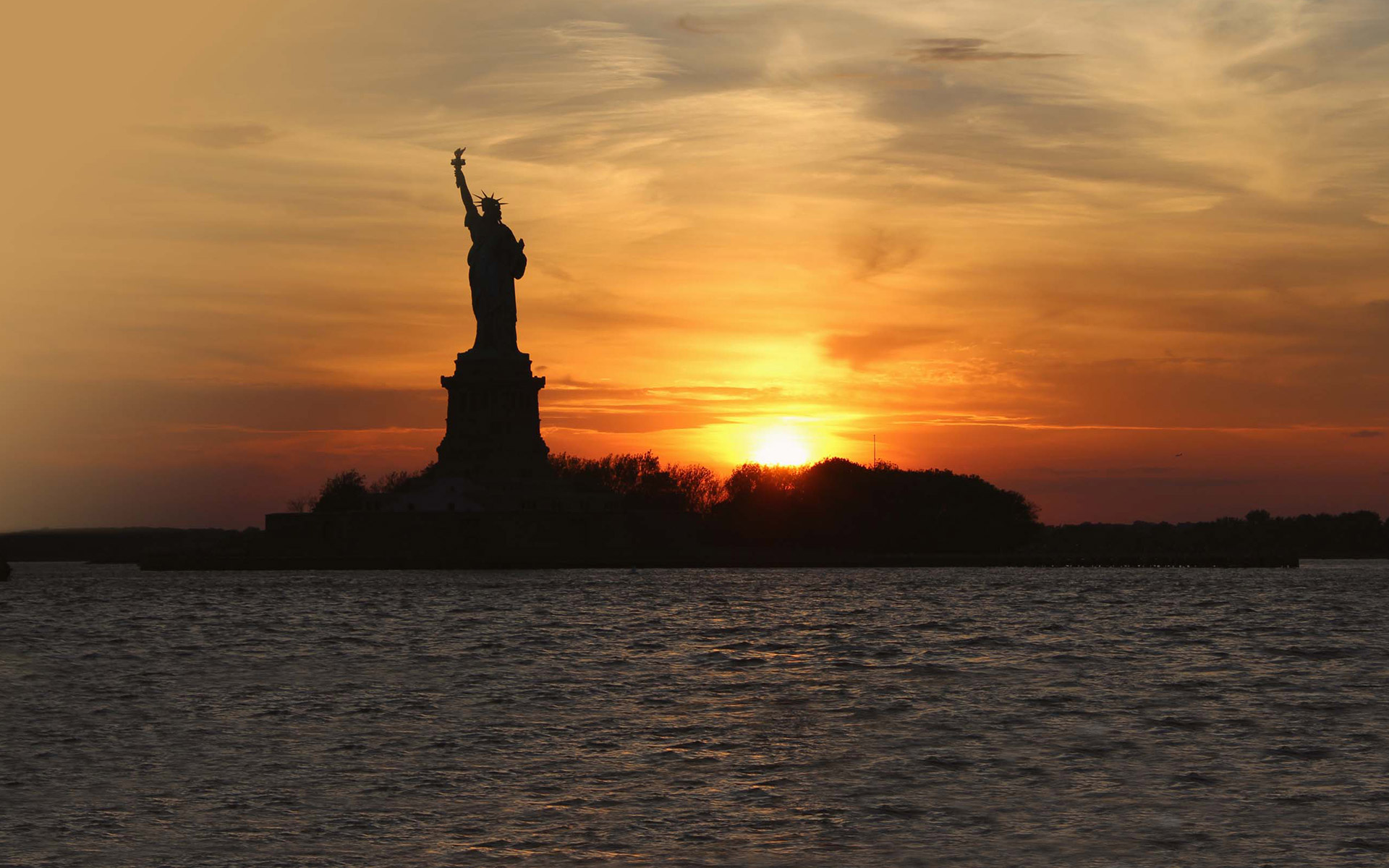 the sunsets behind the statue of liberty on our Sunset Cruise