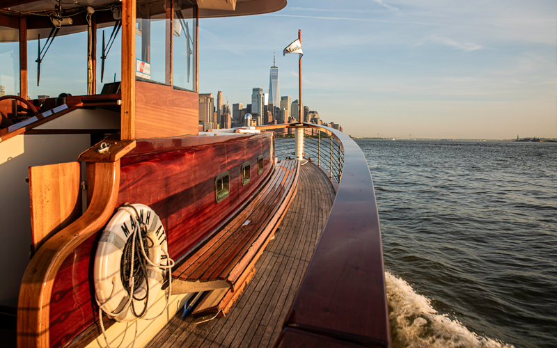 Bow of a classic yacht cruising through NY Harbor with the NYC Skyline in the background