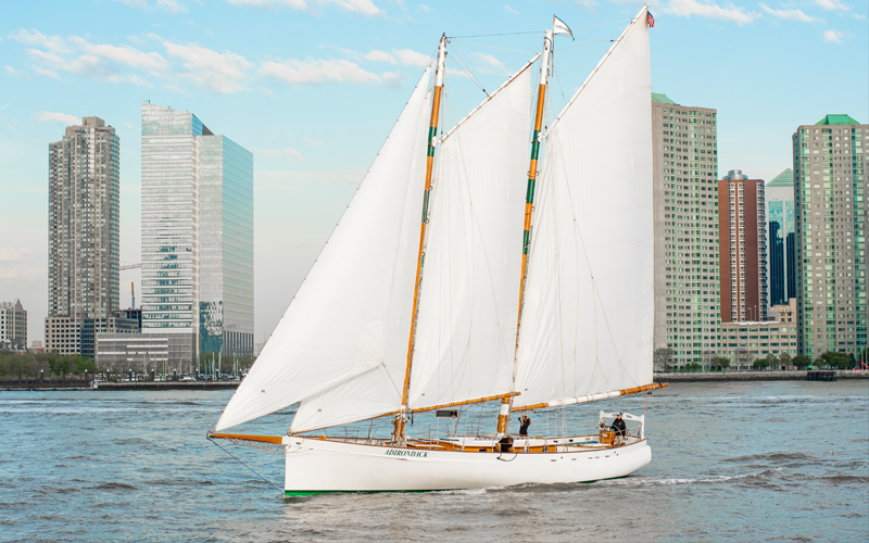Schooner Adirondack sailing on the Hudson River with the NYC skyline in the background.
