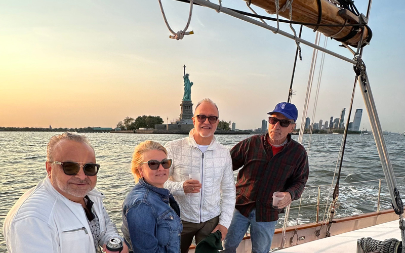 Customers enjoying drinks on the deck of Schooner Adirondack with the Statue of Liberty behind them