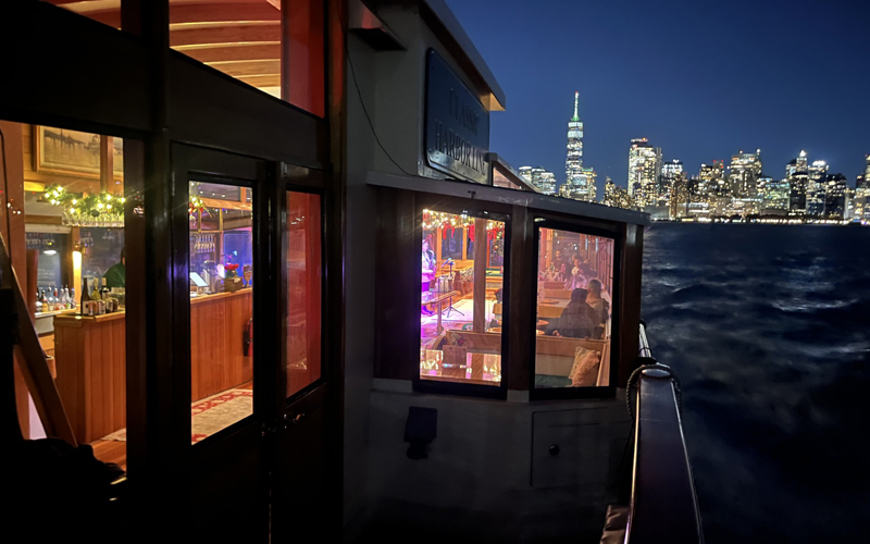 Outside deck of a classic yacht with the NYC Skyline lit up at night