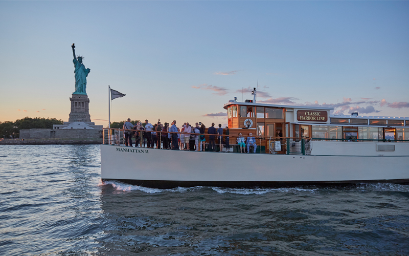 Yacht Manhattan II with guests on deck with the Statue of Liberty behind them