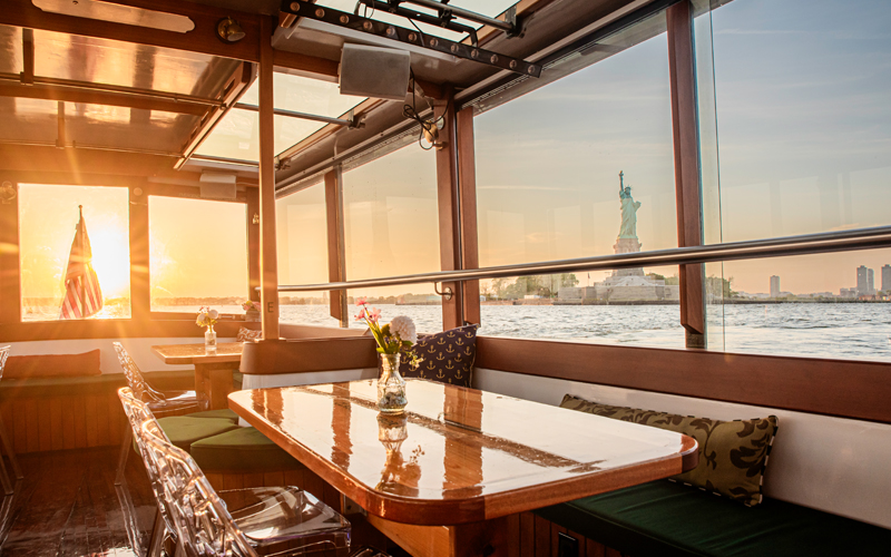 Interior Cabin of Yacht Manhattan with the sun setting outside the window with the Statue of Liberty