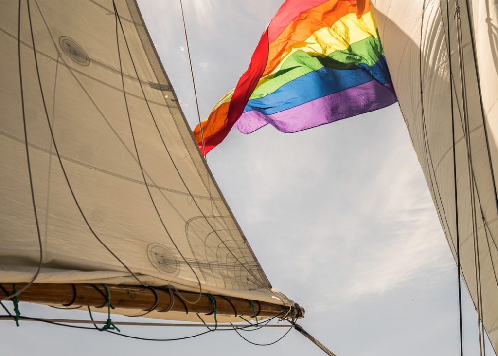 Between the sails of Classic Harbor Line's schooner the Pride flag waves in the sun.