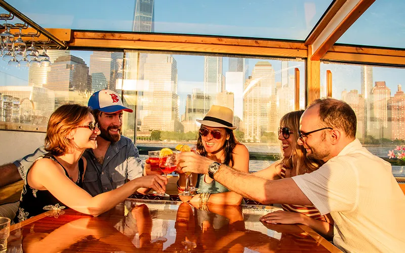 ChampCheeseWeb1 Group of friends sitting at a table inside a classic yacht, cheering drink glasses