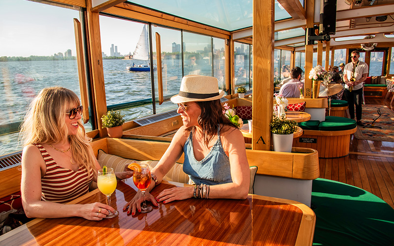 Two woman enjoying drinks and a jazz band playing in the background on a boat.