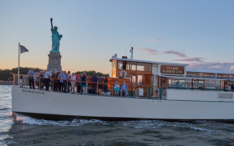 Manhattan II in front of the Statue of Liberty with guests on the bow of the boat.