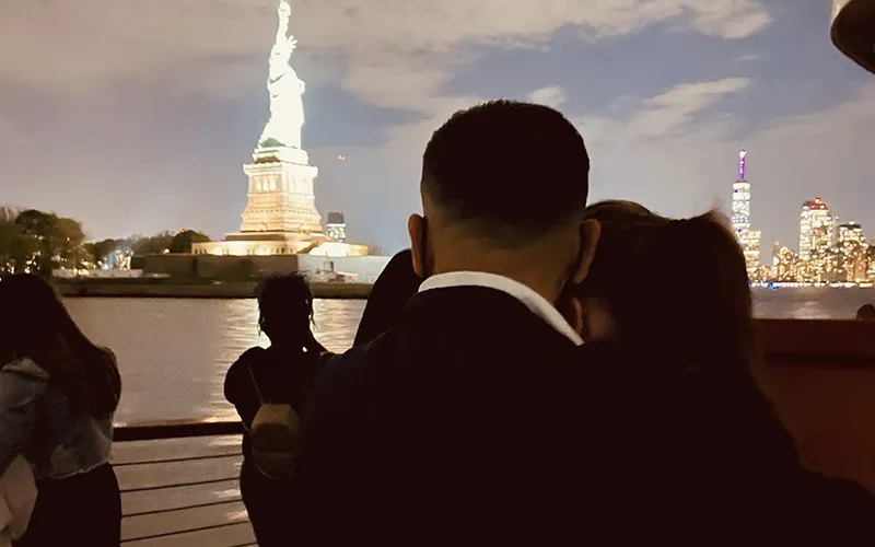 CityLightsSerenade2 Couple on the bow of a boat with the Statue of Liberty in the background.