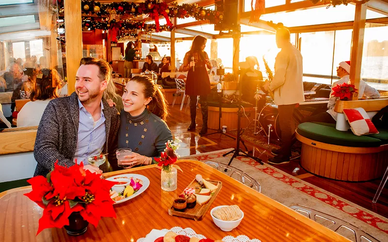 Couple in the grand salon of Yacht Manhattan II decked out in holiday decor and a band playing in the background