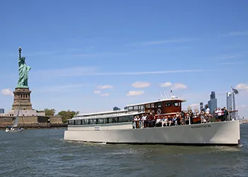 Yacht Manhattan III in front of the Statue of Liberty on a sunny day