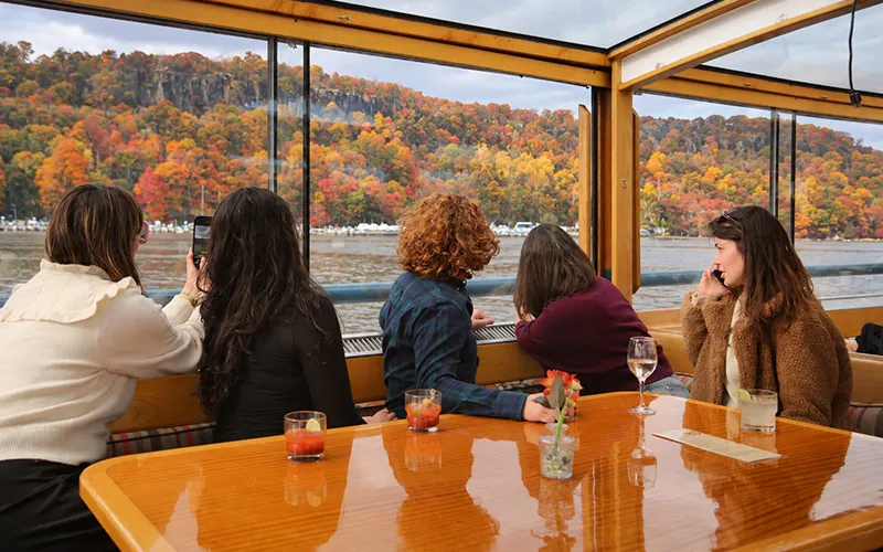 Group of friends sitting at a table on a yacht, looking out the window at the Grand Palisades in the background