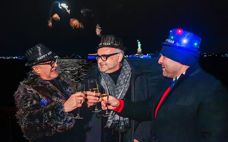 NewYear18 Three men enjoying champagne on New Year's Eve in NY Harbor with the Statue of Liberty and Fireworks in the background