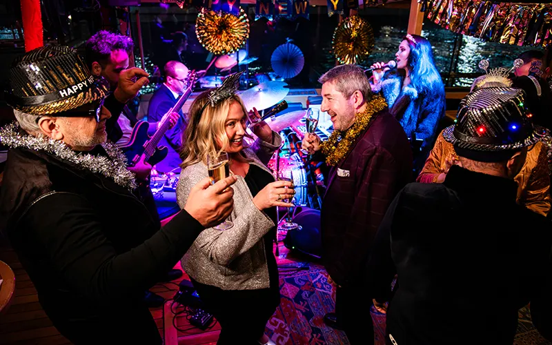 Guests dancing in the grand salon of Yacht Manhattan II with a band playing in the background with New Year's Eve decorations all around