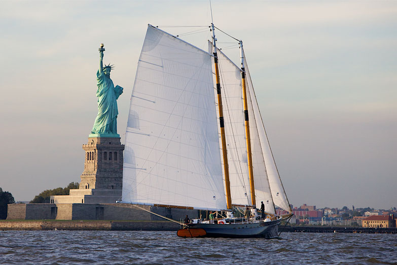 Schooner America 2.0 stern shot of the boat in front of the Statue of Liberty during the day