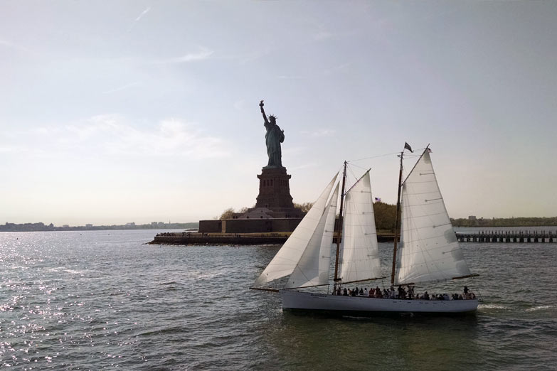 Full boat shot of the schooner Adirondack sailing past the Statue of Liberty in NY Harbor