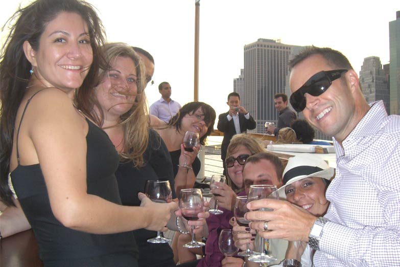 Group of friends on the bow of Yacht Manhattan clinking their drinks and smiling at the camera
